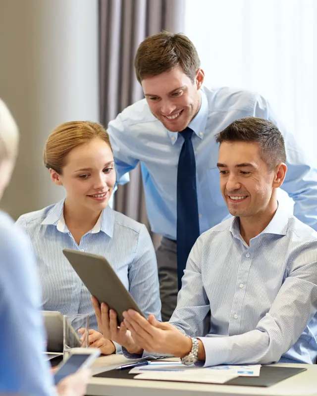 Trois collègues souriants qui consultent une tablette autour d’une table de travail